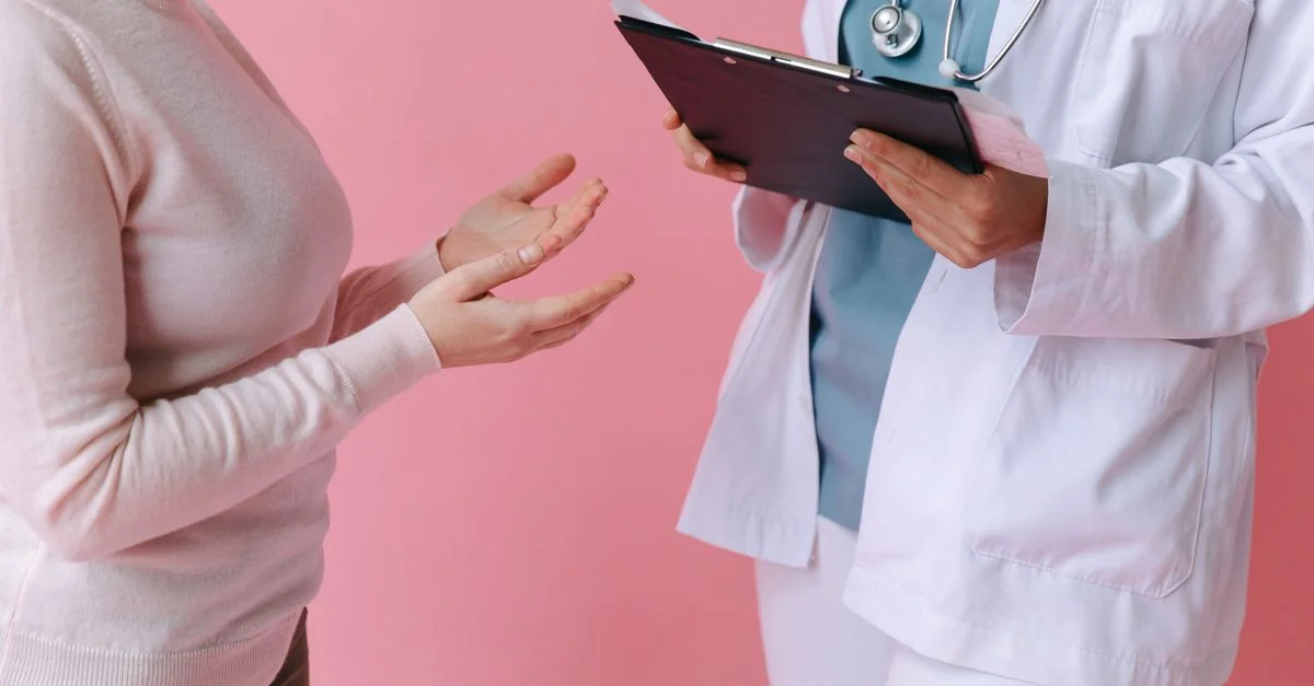 Primer plano de un paciente consultando a un médico con una clipboard en un entorno médico.