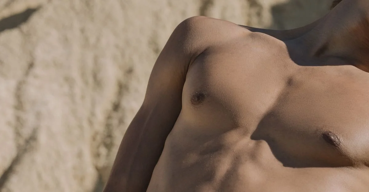 Primer plano del torso de un hombre sin camisa con un fondo arenoso.