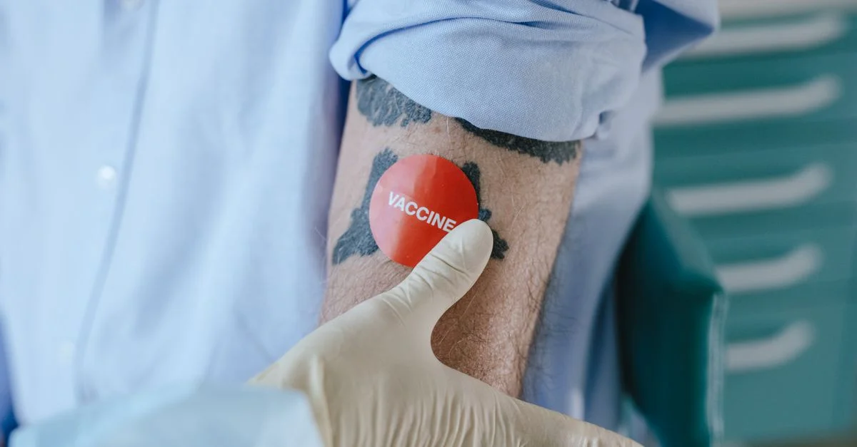Un profesional de salud aplica una etiqueta de vacuna en un brazo tatuado en un entorno médico.