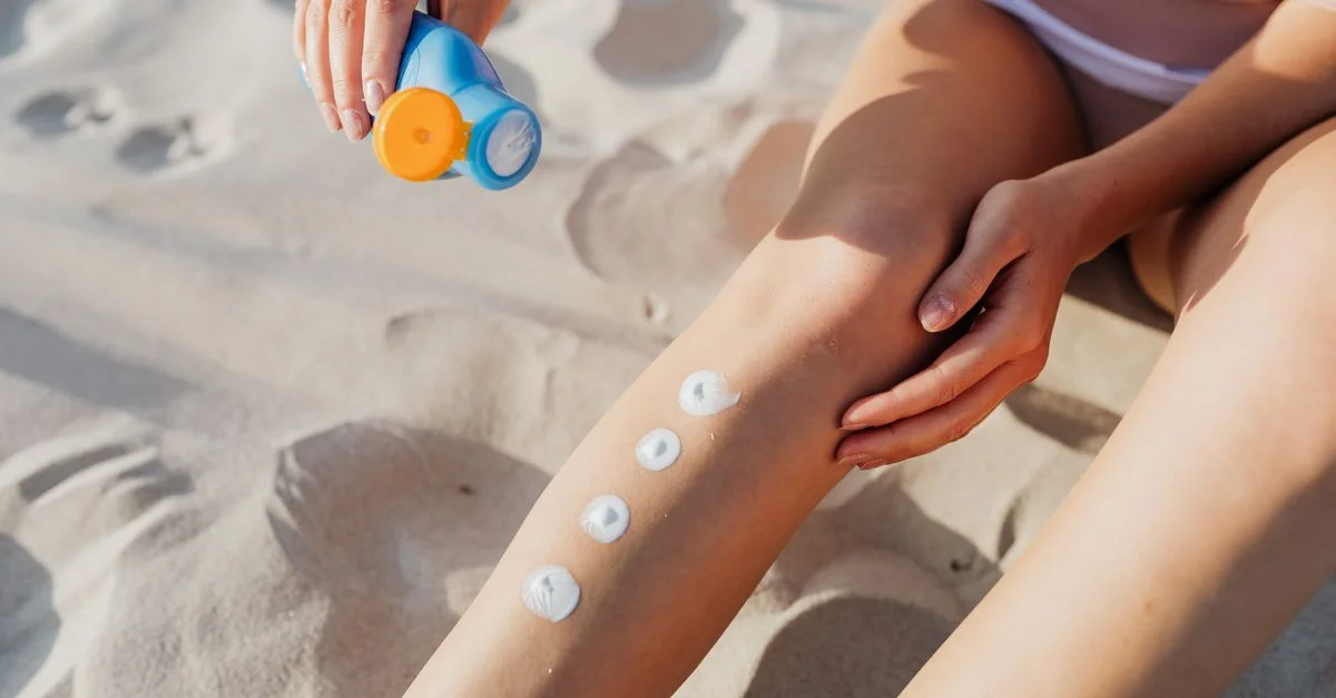 Primer plano de la aplicación de protector solar en las piernas en la playa para proteger la piel.
