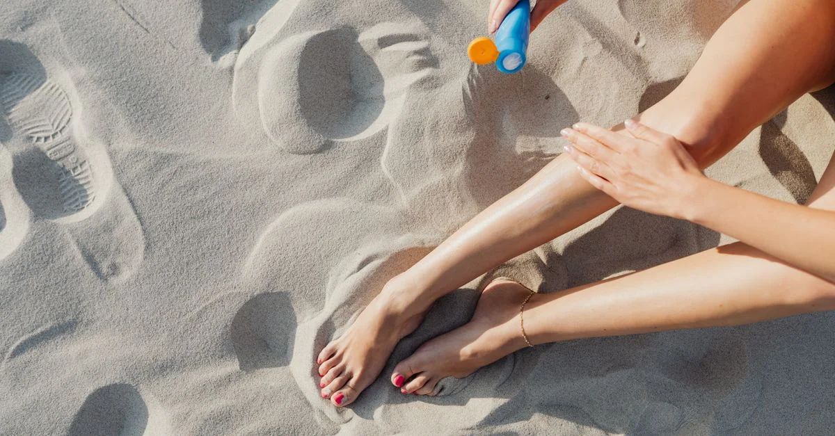 Primer plano de las piernas de una mujer mientras se aplica protector solar en un día soleado en la playa.