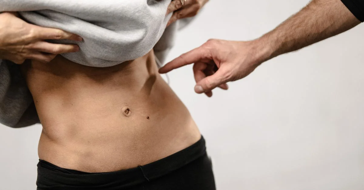 Un primer plano íntimo del área abdominal tonificada de una persona con una mano apuntando, enfatizando la aptitud física.