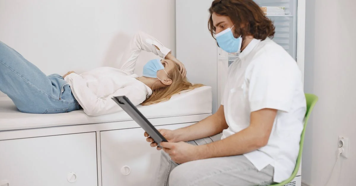 Doctor consultando a paciente con mascarillas en una sala de examen médico, discutiendo el plan de salud.