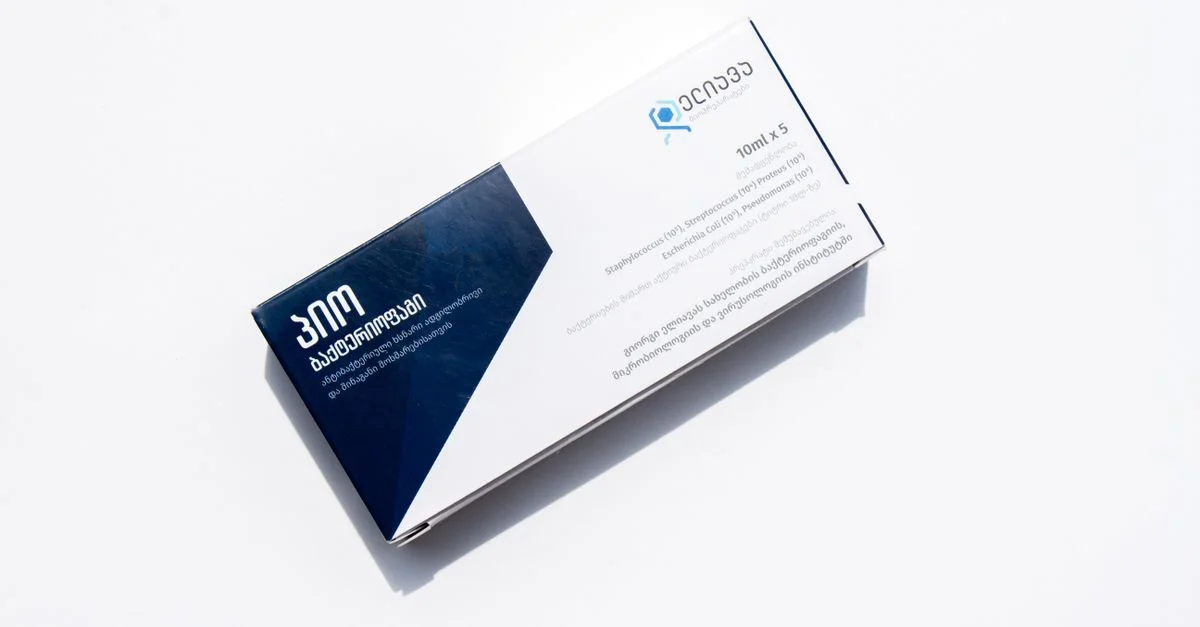 Una caja de medicamentos con texto en inglés y georgiano, aislada sobre un fondo blanco para propósitos de salud.