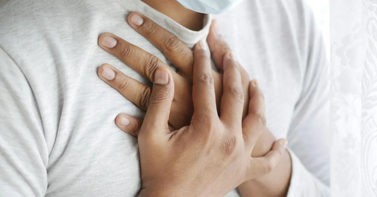 Imagen en primer plano de una persona enmascarada sosteniendo el pecho, simbolizando preocupaciones de salud.