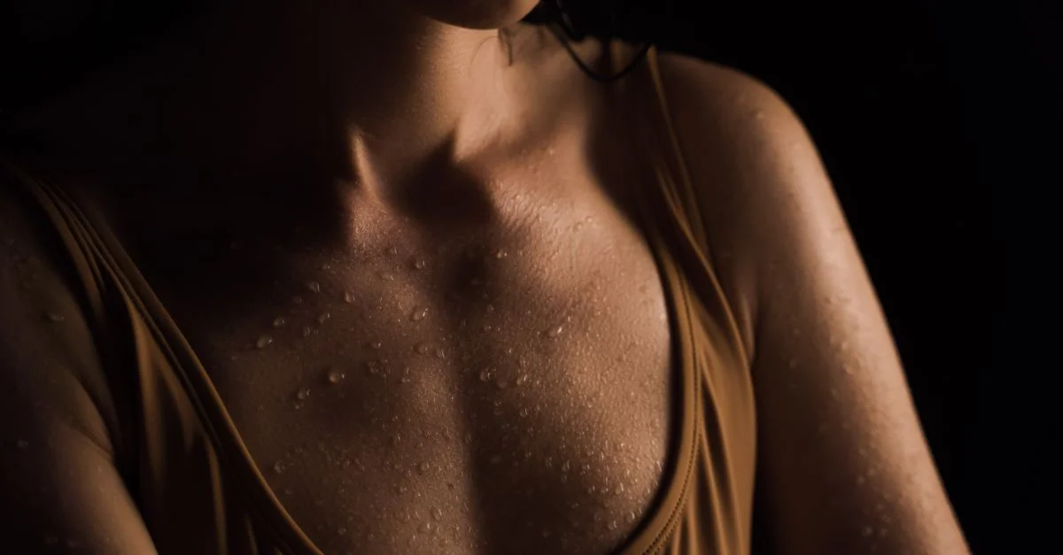 Primer plano de la piel húmeda de una mujer con gotas de agua, contra un fondo oscuro.