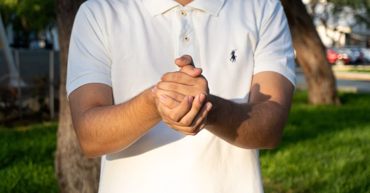 Primer plano de un hombre aplaudiendo sus manos en un parque soleado en Piura, Perú, vistiendo una camiseta polo blanca.