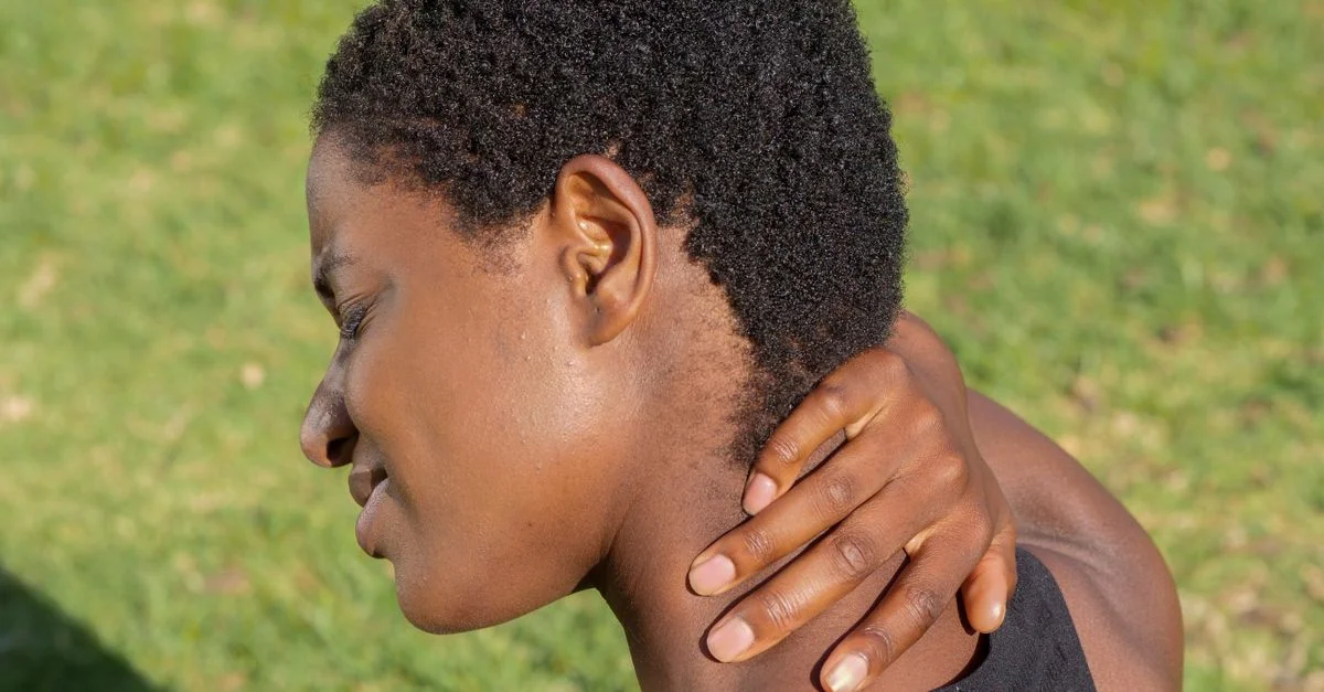 Mujer afroamericana tocándose el cuello al aire libre, experimentando incomodidad.