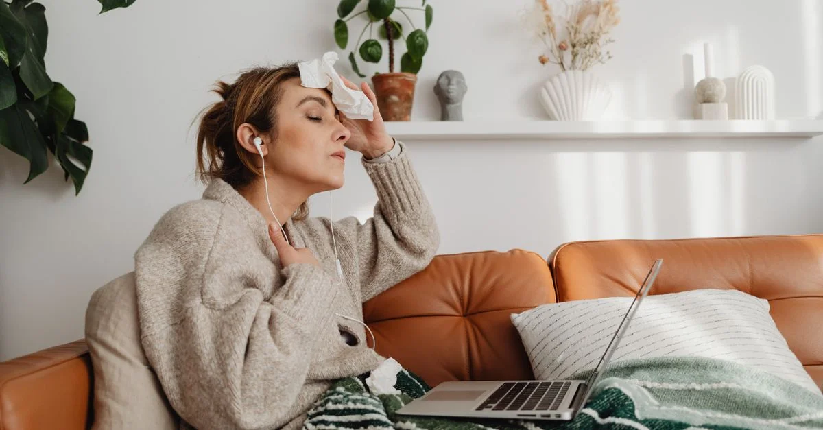 Mujer sentada en el sofá con un portátil y auriculares, luciendo relajada en interiores.
