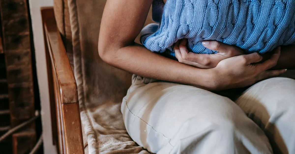 Una mujer sentada en interiores sosteniendo una almohada contra su estómago, indicando incomodidad o dolor.