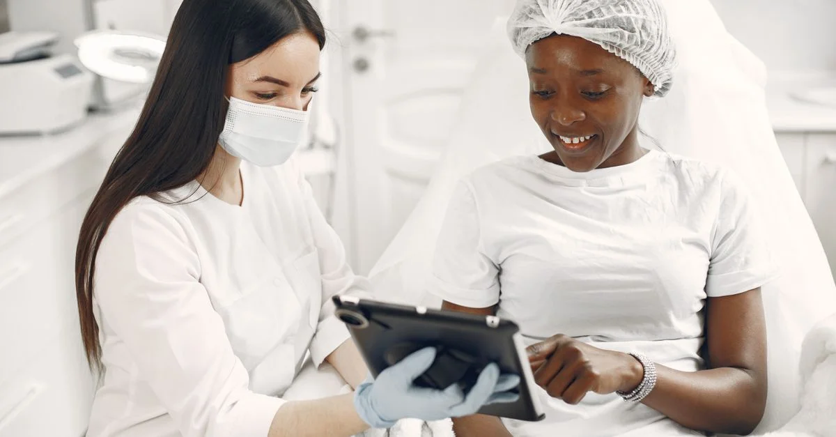Paciente sonriente y dermatólogo usando la tableta durante la consulta de cuidado de la piel.
